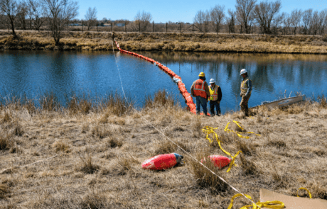 Orange oil containment boom being deployed across a waterway by environmental response crews to help control oil and floating pollutants.