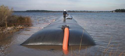 Large geotextile dewatering tube installed along a shoreline to contain dredged sediment and filter water during dewatering operations.