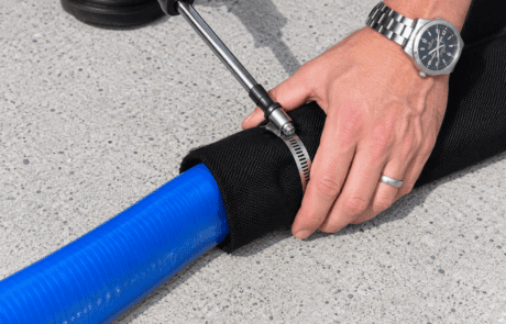 Close-up of a dewatering tube fill port being secured around a discharge hose for pumping sediment-laden water into a geotextile dewatering system.